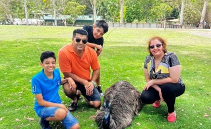 A man, woman and two boys pose on the grass next to a seated emu or ostrich at a wildlife park